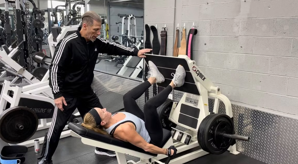 A BAK To Life Fitness trainer coaching a member through a leg press set